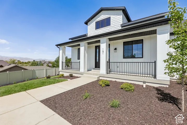 Contemporary two-story exterior featuring white siding, black-framed windows, a covered front porch with black railings, and a dormer window
