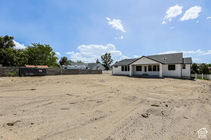 Expansive lot with a newly constructed residence featuring a covered patio, multiple windows, and a dark shingle roof