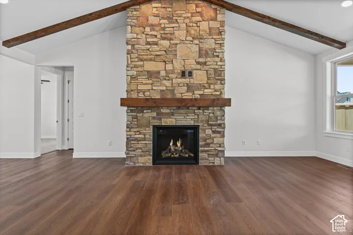 Stone-clad fireplace with a wood mantle, vaulted ceilings, exposed ceiling beams, and wood-finish flooring
