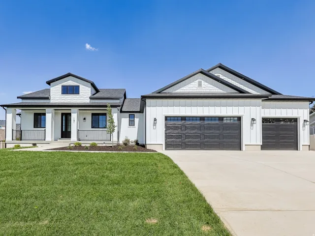 Modern farmhouse exterior with white vertical and horizontal siding, dark roof, and covered front porch with black railings