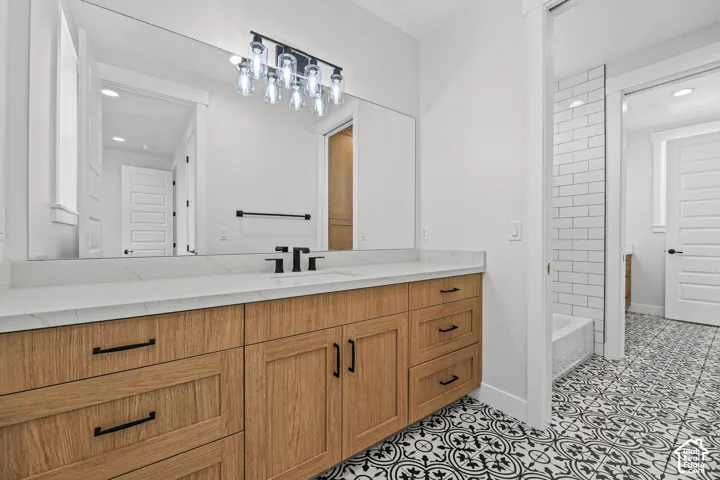 Wood-finish vanity with black hardware, white countertop, and patterned floor tile