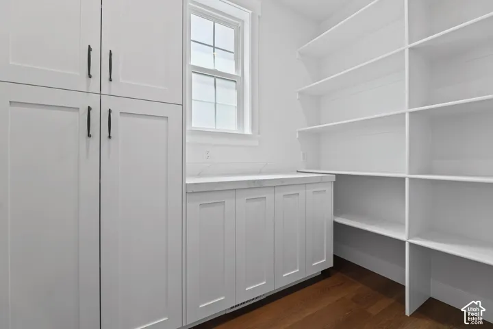 Built-in cabinetry with dark hardware, white countertop, white subway tile backsplash, window, and wood-finish flooring