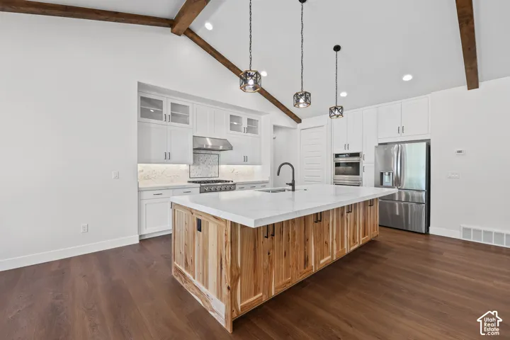 Kitchen with vaulted ceilings, exposed wood beams, wood-finish flooring, a large island with a light-toned countertop, and stainless steel appliances