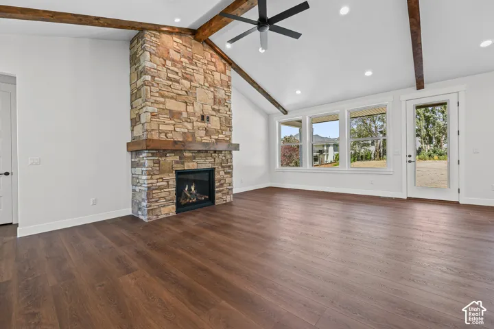 Vaulted ceiling with exposed wood beams, stone-clad fireplace with wood mantel, wood-finish flooring, recessed lighting, and multiple windows