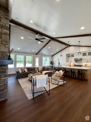 Vaulted ceiling with exposed wood beams, wood-finish flooring, stone-clad fireplace, recessed lighting, and a kitchen island with seating