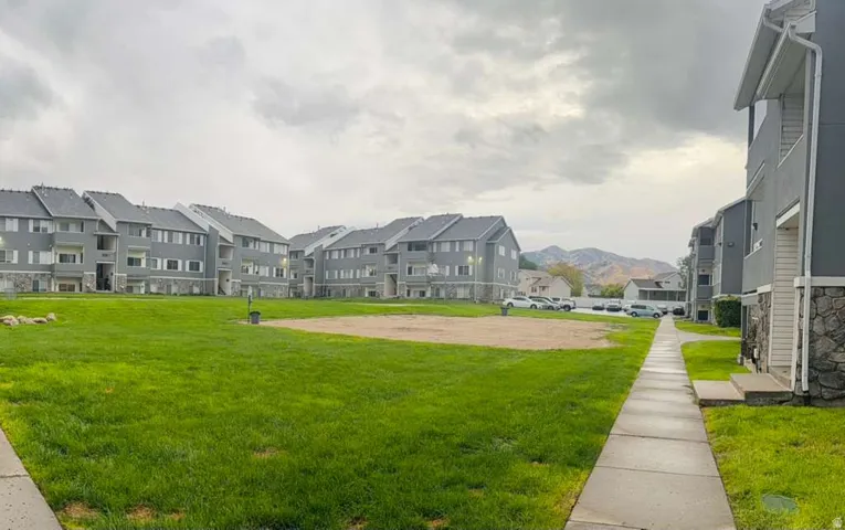 Expansive green lawn area with walking path, surrounded by multi-story residential buildings featuring stone veneer and balconies