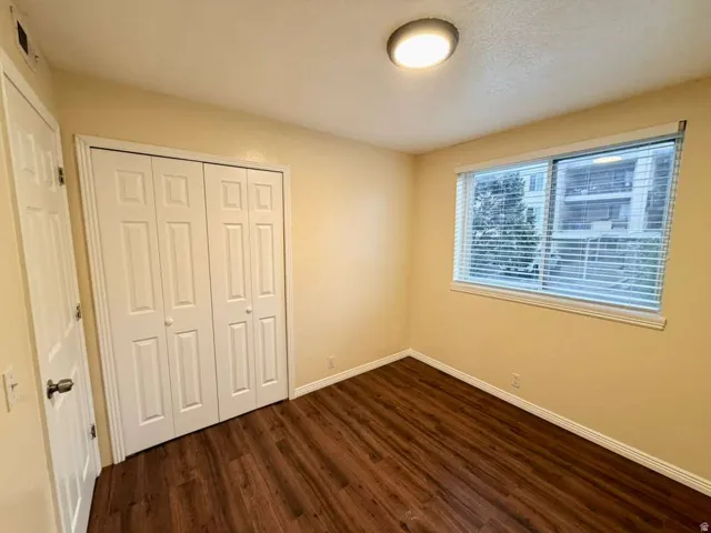 Wood-finish flooring with white baseboards, a window with horizontal blinds, and a built-in closet with bi-fold doors