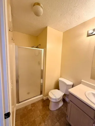Enclosed shower with a glass door, vanity with an integrated sink, wall-mounted light fixture, and tiled flooring