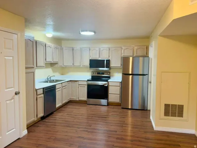 Kitchen featuring wood-finish flooring, stainless steel appliances, light-toned cabinetry, and white countertops