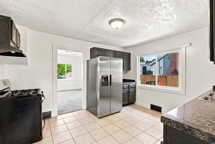 Kitchen featuring dark cabinetry, stainless steel refrigerator, granite-finish countertops, tiled flooring, and a gas range with an overhead microwave