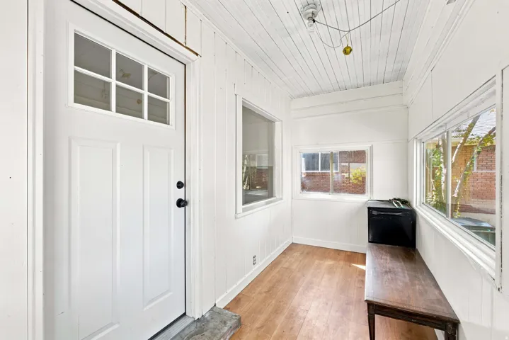 White paneled door with glass insert, wood-finish flooring, and multiple windows