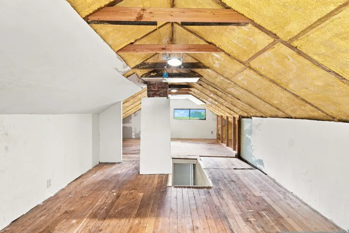 Exposed wood-beam ceiling with insulation, wood-finish flooring, and natural light from a window