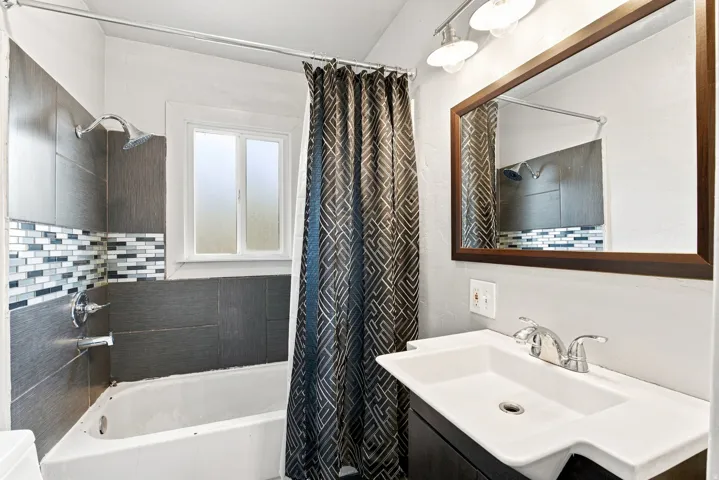 Full-size bathtub with a mosaic tile accent, modern vanity with an integrated sink, and an overhead vanity light fixture