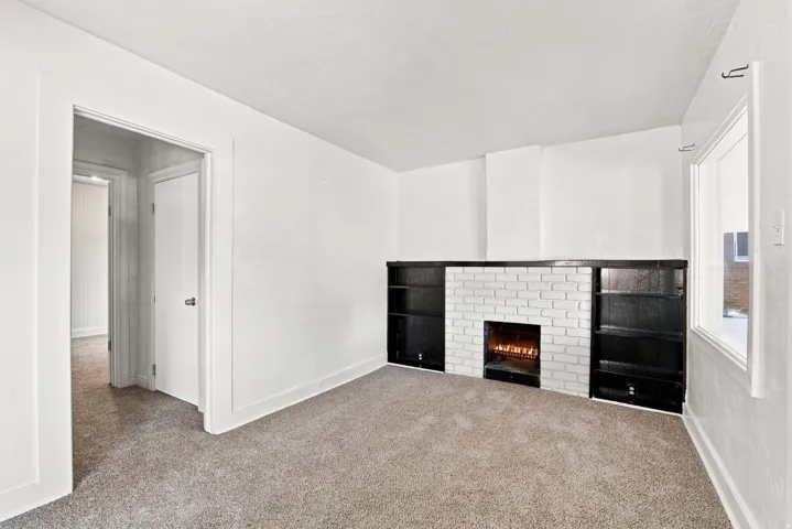White brick fireplace with dark built-in shelving, carpeted flooring, and white painted walls