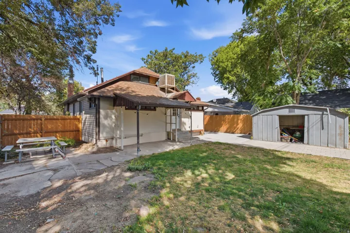 Spacious backyard featuring a covered patio, paved areas, a detached shed, and a privacy fence