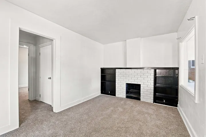 Carpeted room featuring a white brick fireplace, built-in shelving, and a window