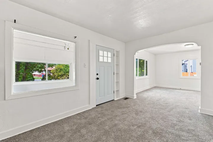 White interior door with glass panels, built-in shelving, gray carpet, white walls, and arched doorway