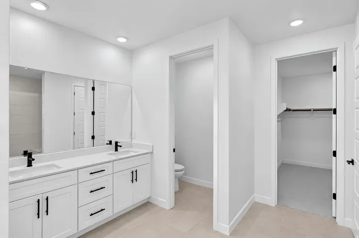 Double vanity with white cabinetry and matte black hardware, integrated sinks, large wall-mounted mirror, recessed lighting, and tile flooring