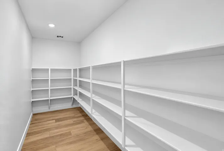Spacious pantry featuring extensive built-in shelving, wood-finish flooring, and a recessed ceiling light
