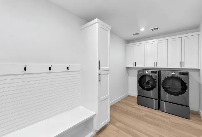 White shaker-style cabinetry with matte black hardware, built-in mudroom bench, beadboard wall paneling, and wood-finish flooring