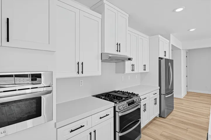 White shaker cabinetry, stainless steel appliances, integrated wall oven, countertop range, and wood-finish flooring