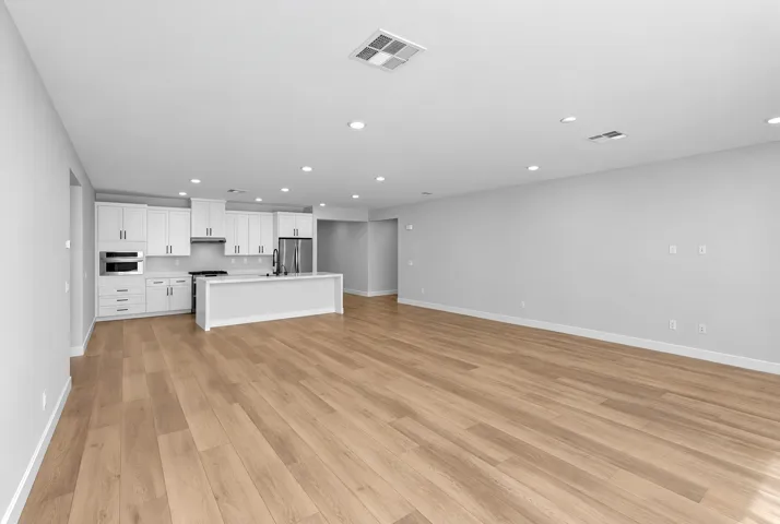 Open-concept living space with wood-finish flooring, recessed lighting, and a kitchen featuring white cabinetry, stainless steel appliances, and a central island