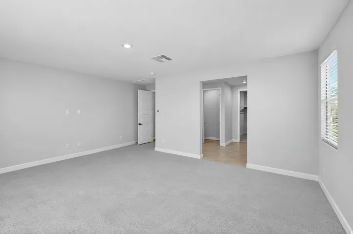 Expansive room featuring light gray carpeting, recessed lighting, and a window with blinds