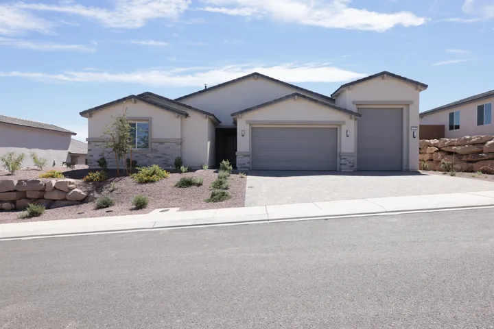 Stucco exterior with stone accenting, an attached two-car garage, an additional attached one-car garage, and a paver driveway