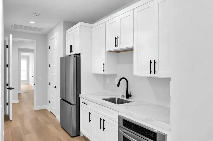 Contemporary kitchen featuring white cabinetry with black hardware, a stainless steel refrigerator, and wood-finish flooring