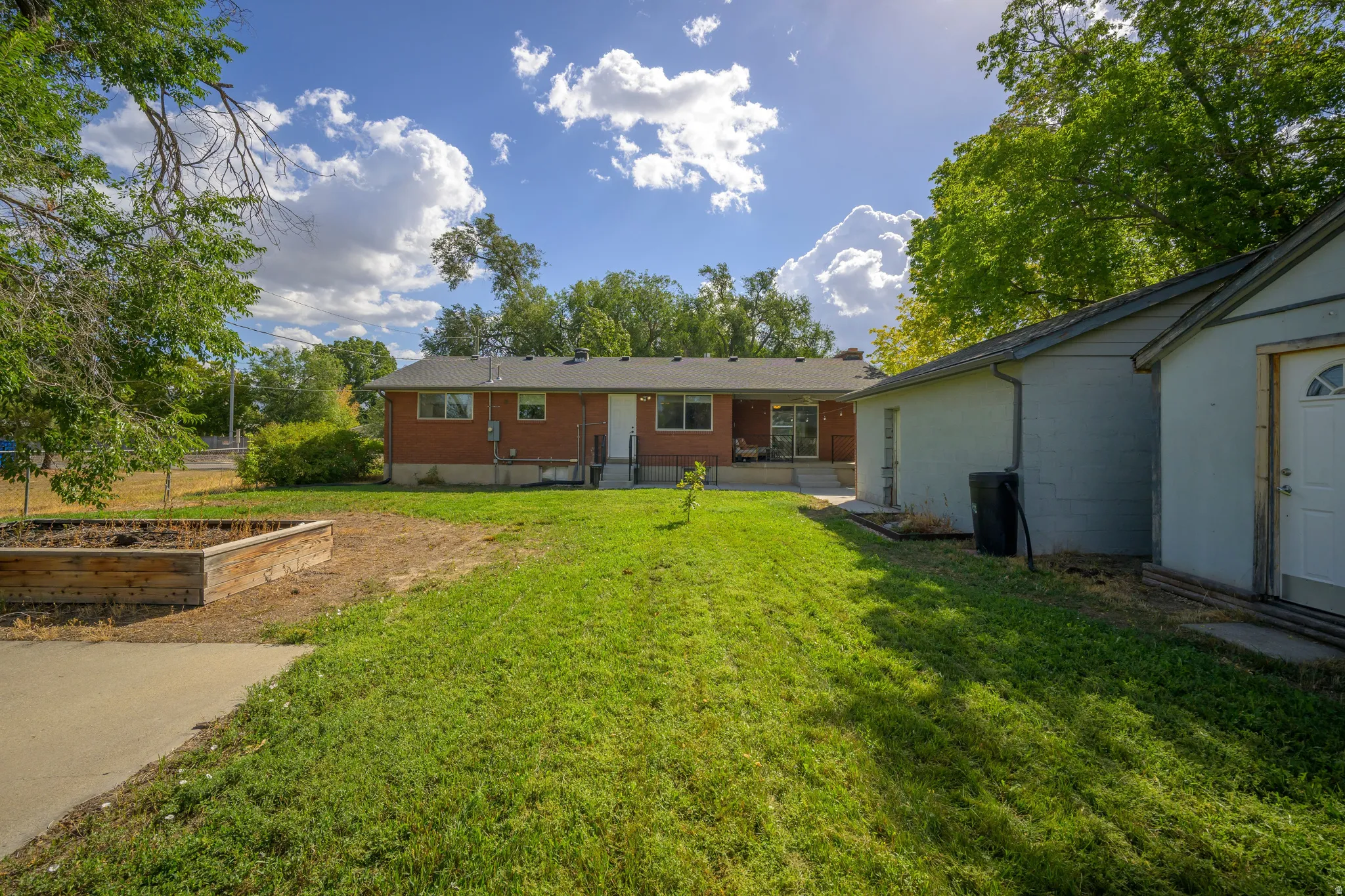 Expansive backyard featuring a manicured lawn, an established raised planter bed, and a detached outbuilding