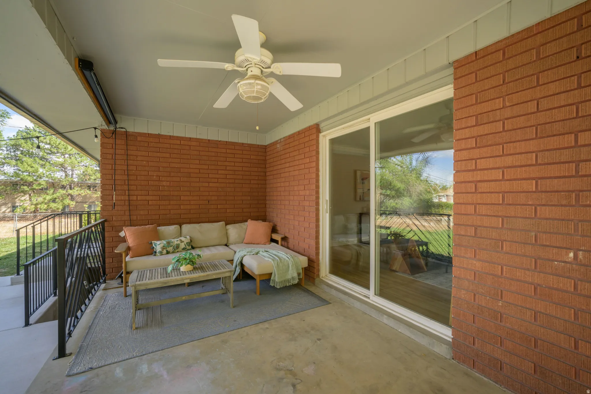 Covered patio with a ceiling fan, brick wall, and sliding glass door
