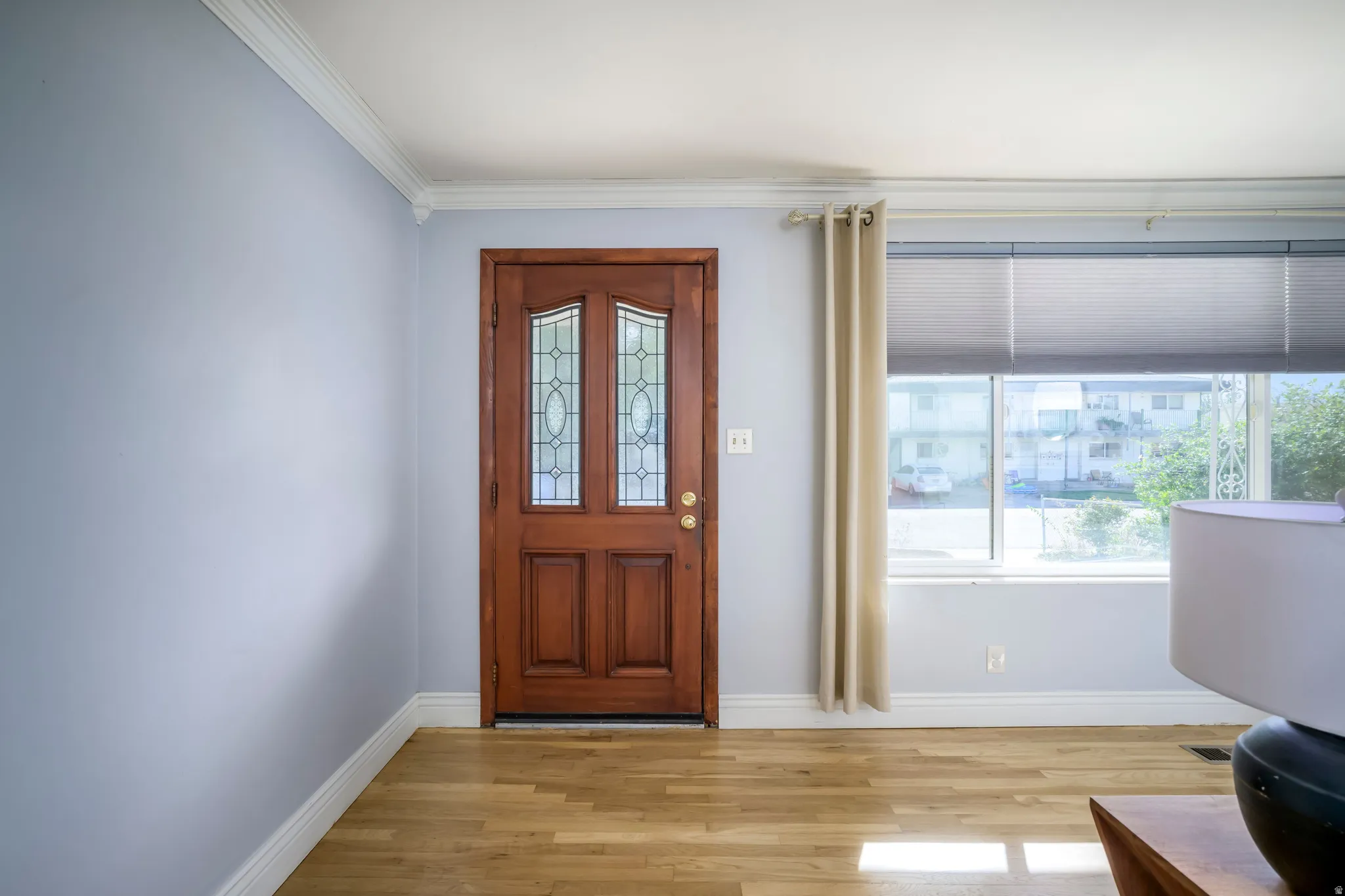Wood-finish flooring with a wood front door featuring decorative glass inserts, crown molding, and a large window