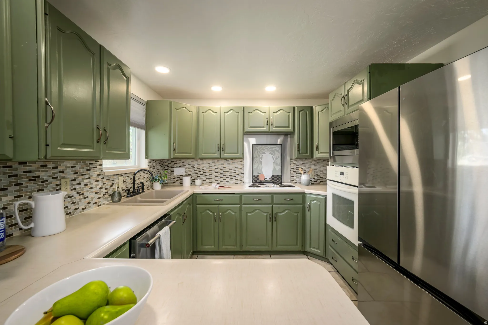 U-shaped kitchen featuring green cabinetry, mosaic tile backsplash, recessed lighting, and stainless steel appliances