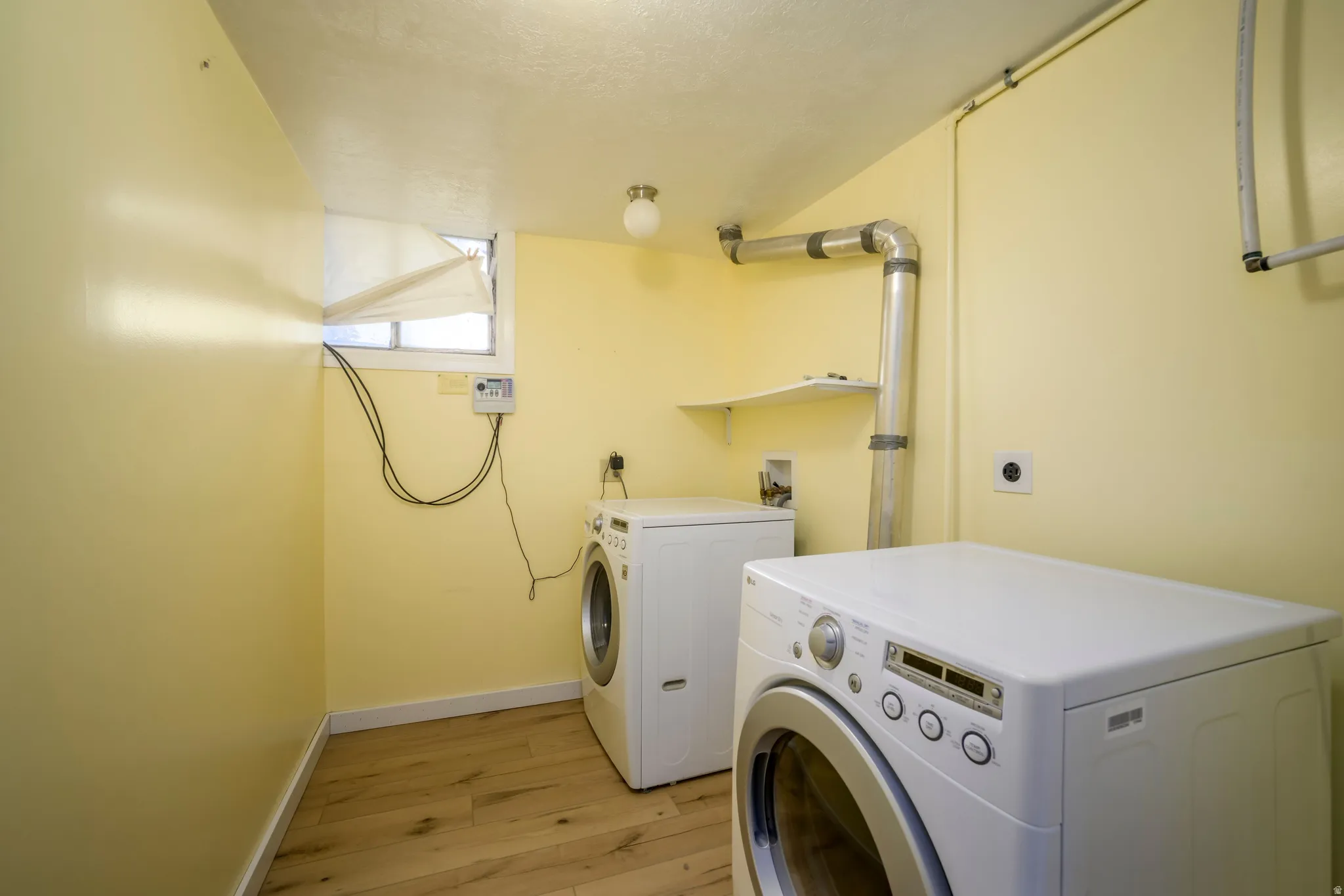 Laundry area featuring wood-finish flooring, a wall-mounted shelf, and a ceiling-mounted light fixture
