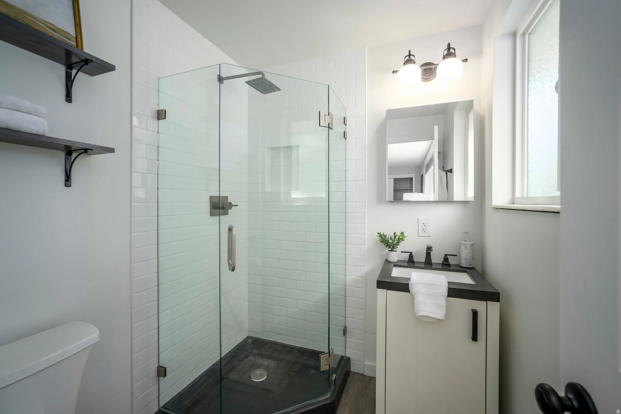 Corner glass-enclosed shower with subway tile surround and dark-finish shower pan