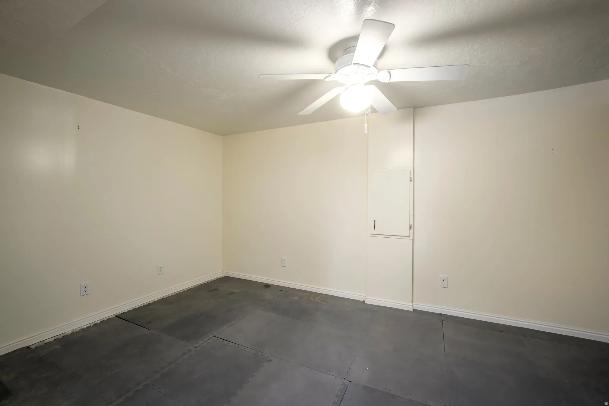 Neutral painted walls with a ceiling fan light fixture and gray flooring