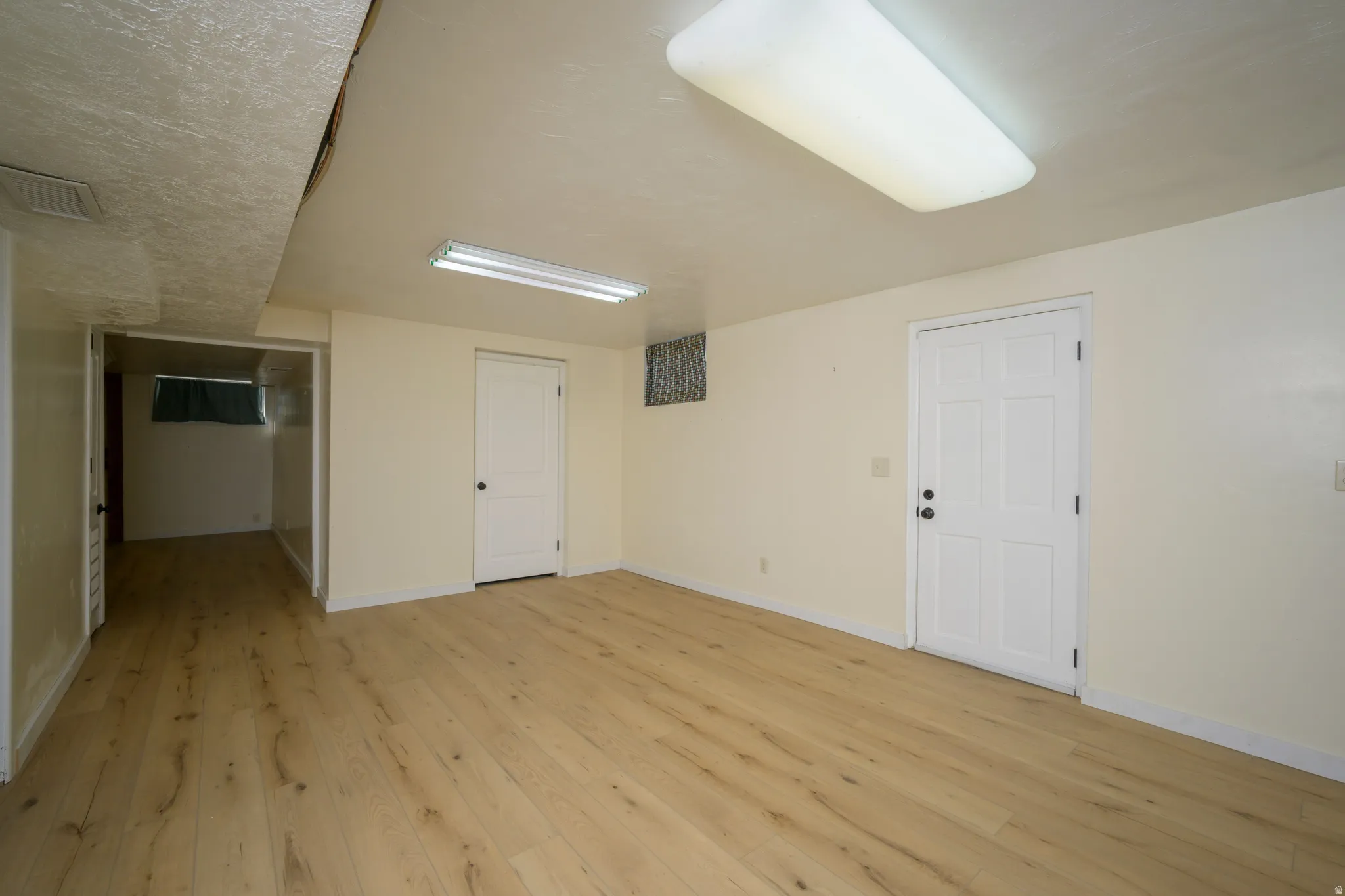 Finished room featuring wood-finish flooring, white paneled doors, and overhead fluorescent lighting