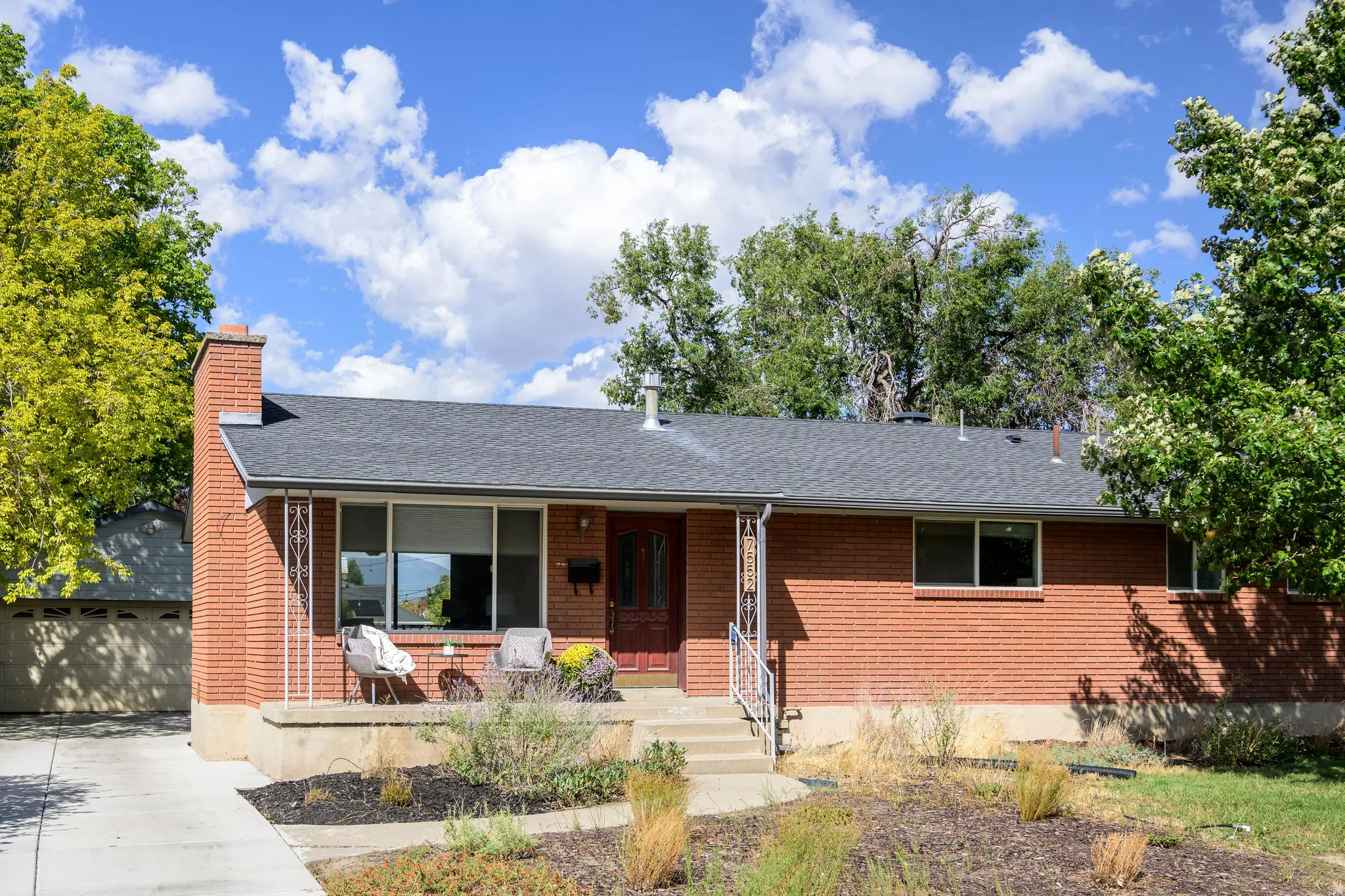 Brick exterior with a dark-shingled roof, featuring a covered front porch, concrete driveway, and established landscape
