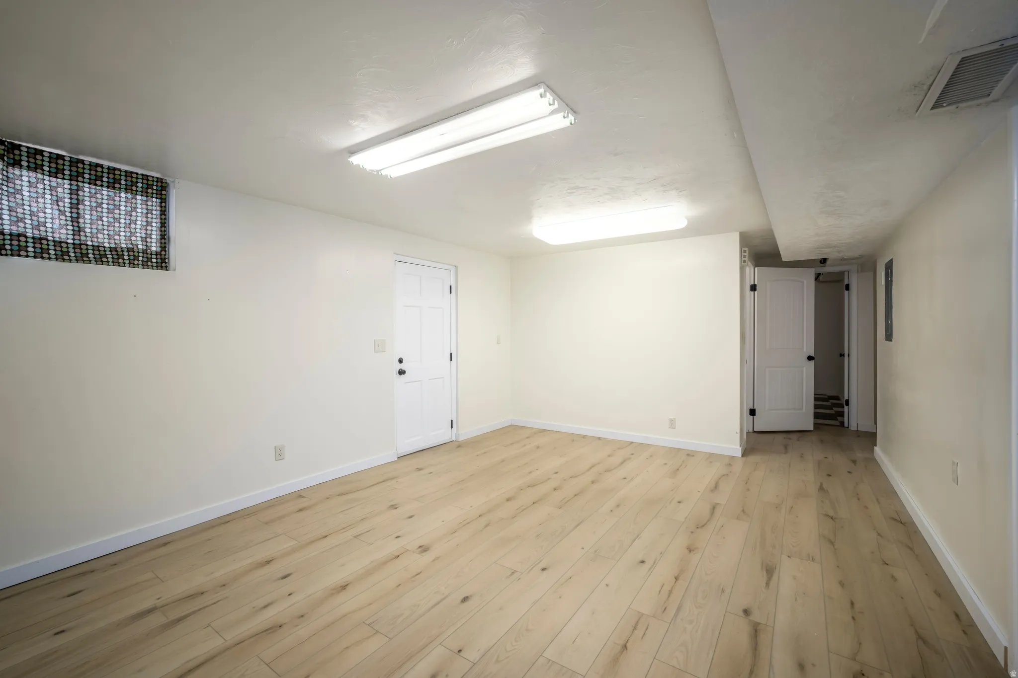 Wood-finish flooring with white baseboards, white walls, and overhead fluorescent lighting