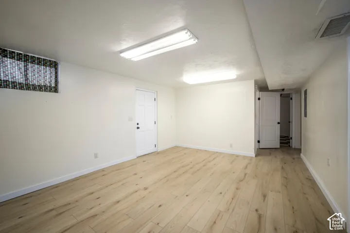 Wood-finish flooring with white baseboards, white walls, and overhead fluorescent lighting