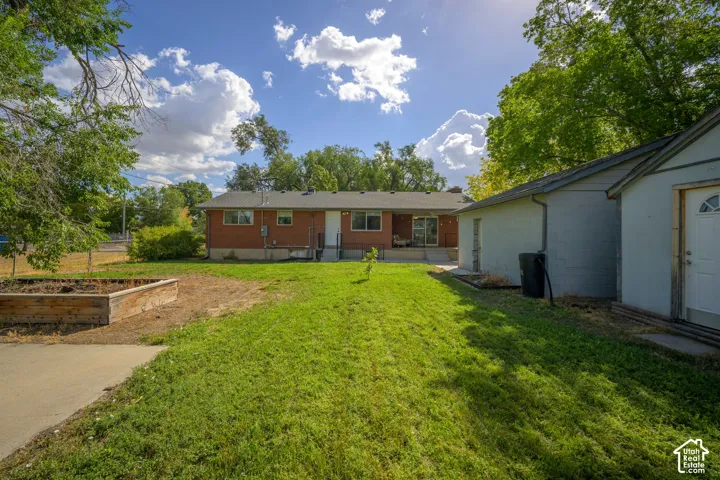 Expansive backyard featuring a manicured lawn, an established raised planter bed, and a detached outbuilding