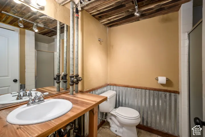 Wood-finish vanity with an oval drop-in sink, corrugated metal wainscoting, exposed wood beam ceiling, and a shower enclosure