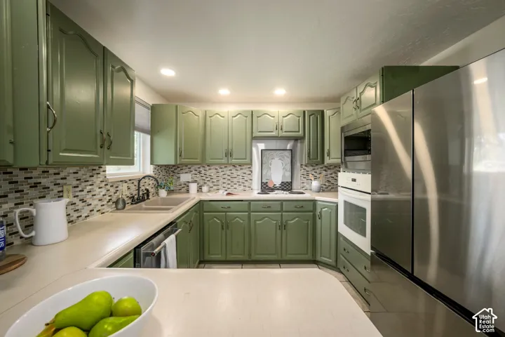 U-shaped kitchen featuring green cabinetry, mosaic tile backsplash, recessed lighting, and stainless steel appliances