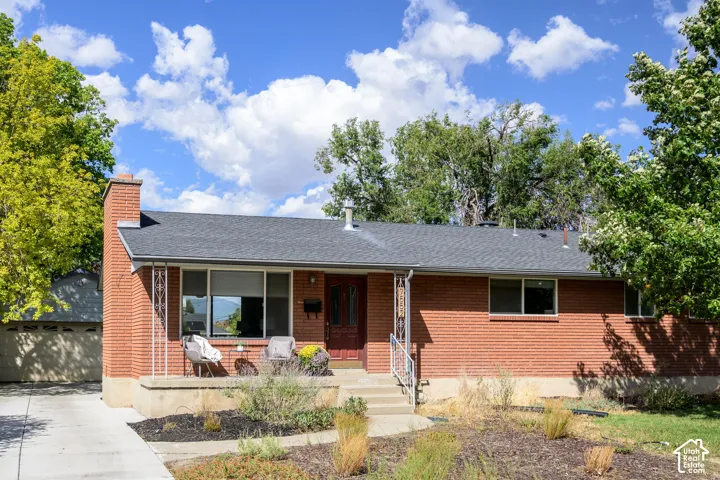 Brick exterior with a dark-shingled roof, featuring a covered front porch, concrete driveway, and established landscape