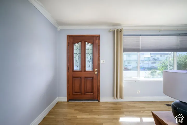 Wood-finish flooring with a wood front door featuring decorative glass inserts, crown molding, and a large window