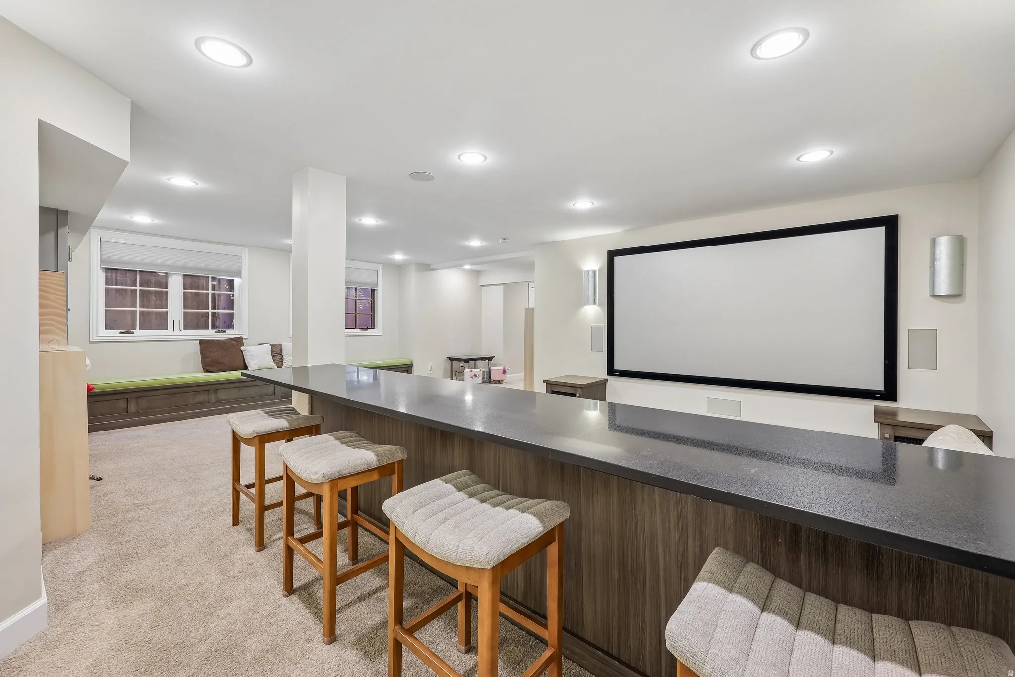 Built-in bar with a dark countertop and wood-finish paneling, a large projection screen, recessed lighting, and built-in window seating