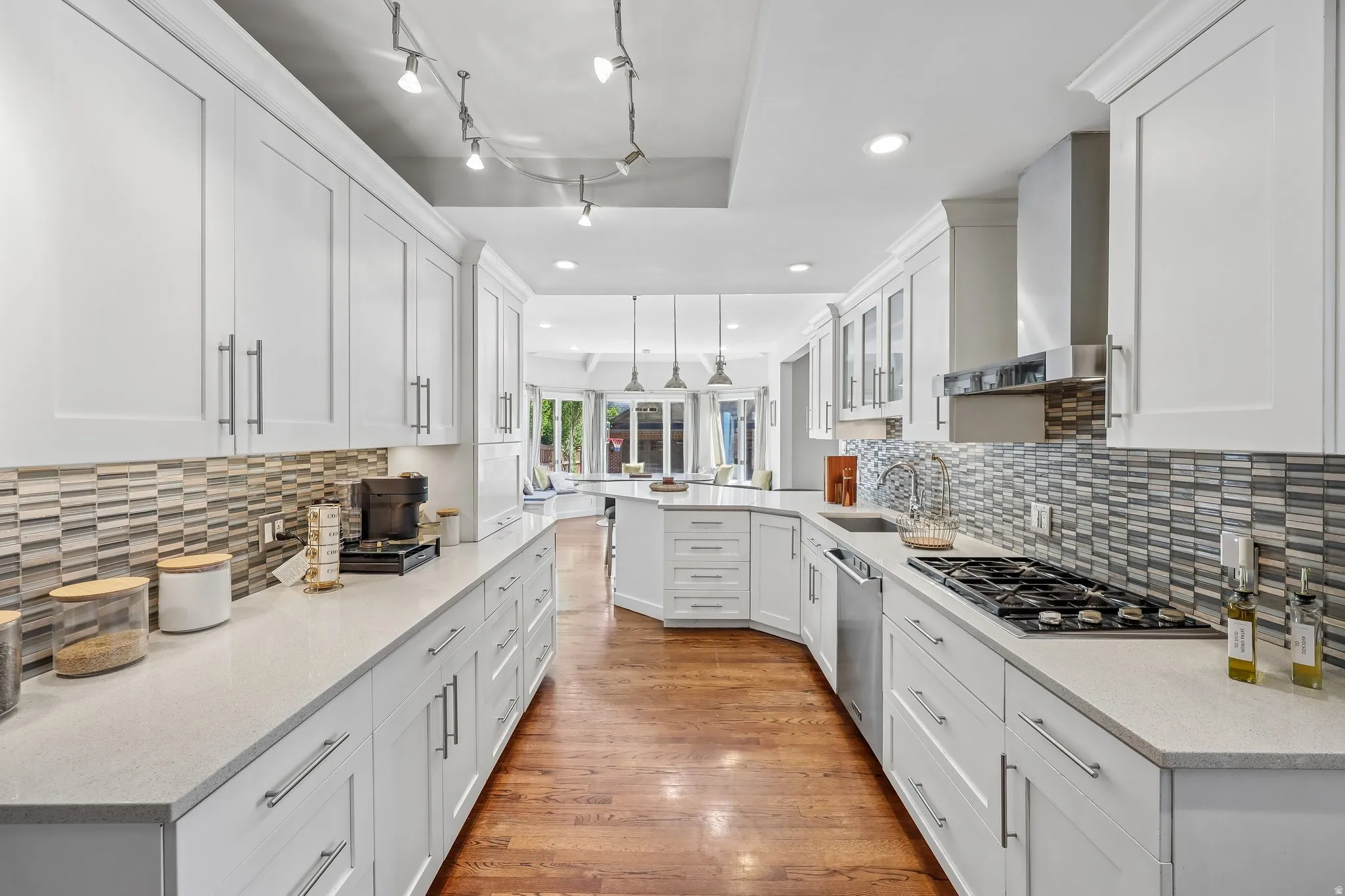 Expansive kitchen featuring white cabinetry, light-toned countertops, a gas cooktop, stainless steel appliances, and a tiled backsplash