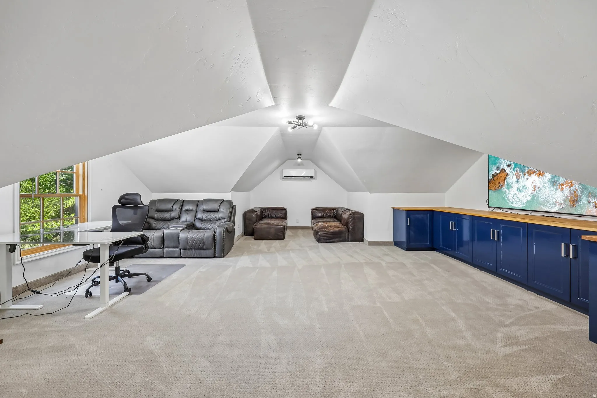 Attic space featuring sloped ceilings, a window with exterior views, built-in blue cabinetry with wood-finish countertops, and light-toned carpeting