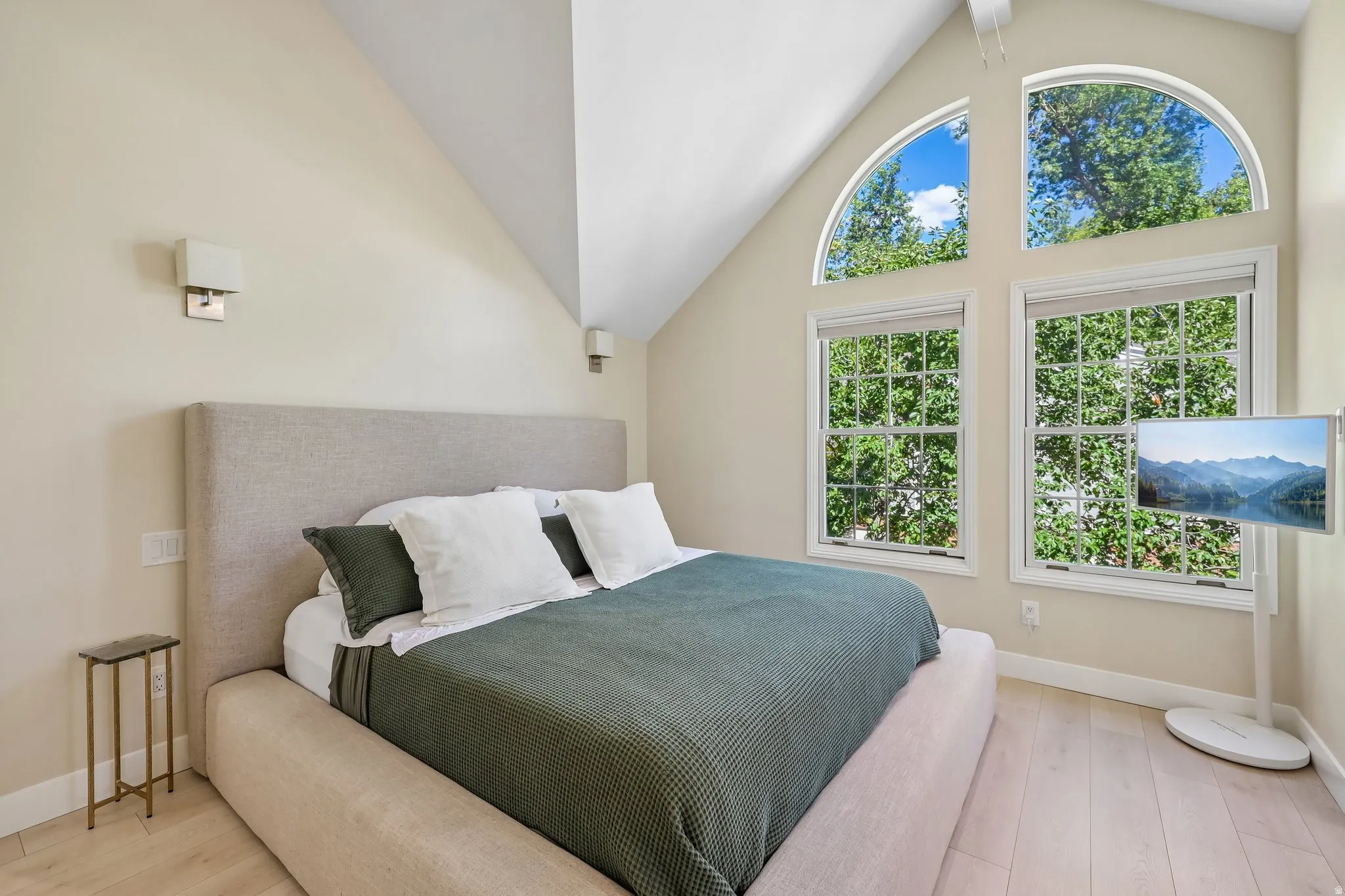 Vaulted ceilings, arched transom windows, dual sash windows with interior grids, wood-finish flooring, and wall-mounted sconces