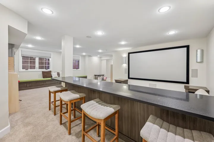 Built-in bar with a dark countertop and wood-finish paneling, a large projection screen, recessed lighting, and built-in window seating